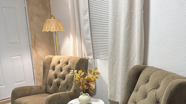 Une pièce comprenant deux fauteuils, une petite table ronde ornée d’un vase de fleurs, une lampe et un tapis blanc à poils longs.