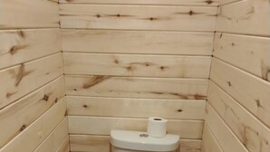Et lille badeværelse med træpaneler, toilet, skraldespand og toiletpapirholder.