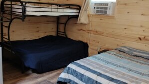 Et træhusværelse med køjesenge, en loftsvifte og et vindue med aircondition.
