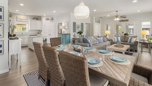 Eine geräumige Küche mit weißen Schränken, ein Essbereich mit Korbstühlen und ein Wohnzimmer mit Sofa und Couchtisch.