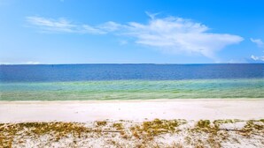 Ein Strand mit klarem türkisblauem Wasser, weißem Sand und wenig Vegetation.