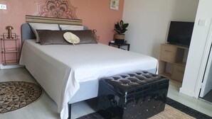 A neatly arranged bedroom with a bed, bedside tables, a TV, and a small plant.