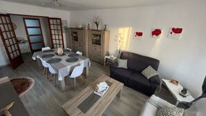 Een woonkamer met een eettafel, bank en salontafel. Er staat een kast met decoratieve objecten en een vaas met bloemen.