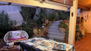 Een terras buiten met een eettafel, omringd door potplanten en een trap naar een hoger niveau.