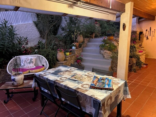 An outdoor patio with a table set for dining, surrounded by potted plants and a staircase leading to a higher level.