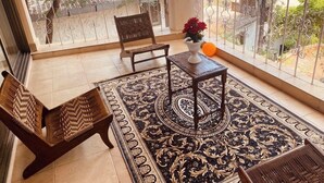 A balcony with a view of the sea, a woven chair, a small table with a vase of flowers, and a patterned rug. - 
Perfect for couples, families, or friends. Book now and unwind in style! (panchgani)