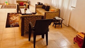 A spacious living room with a sofa set, a coffee table, and a chair. There is a curtain with a birthday banner. - 
Perfect for couples, families, or friends. Book now and unwind in style! (panchgani)