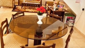 A dining area with a round glass table, four wooden chairs, and a vase of red flowers. - 
Perfect for couples, families, or friends. Book now and unwind in style! (panchgani)