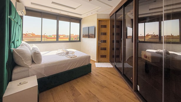 A modern hotel room with a large bed, a sliding glass door to a balcony, and a view of the cityscape.