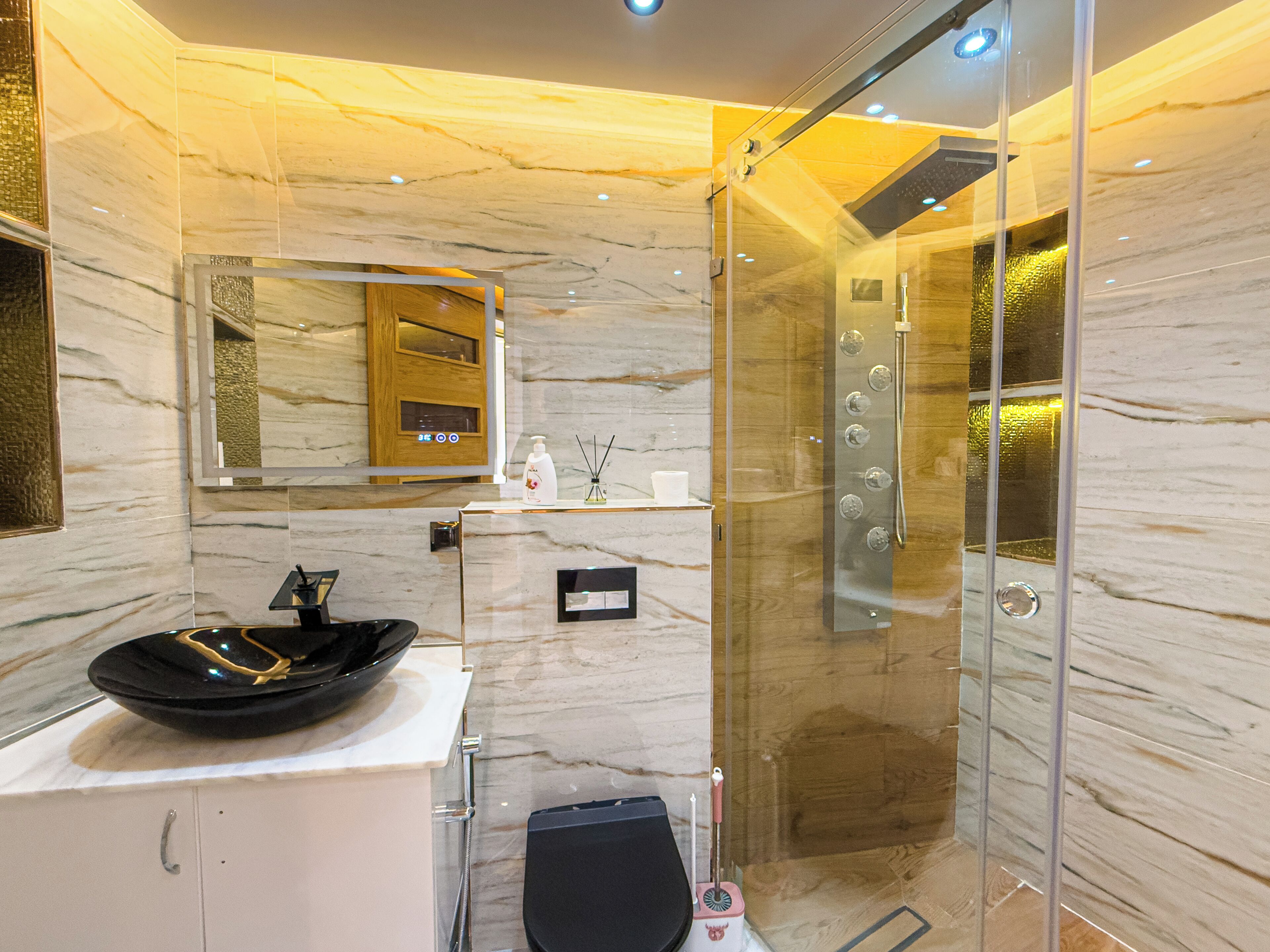 Un baño moderno con ducha envuelta en vidrio, un lavabo negro y un mueble de tocador de madera.