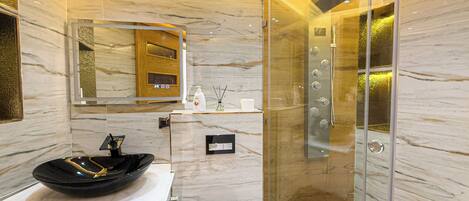 Un baño moderno con ducha envuelta en vidrio, un lavabo negro y un mueble de tocador de madera.