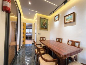 A dining area with a marble floor, wooden table, and chairs. There are framed paintings on the wall and a fire extinguisher on the wall.
