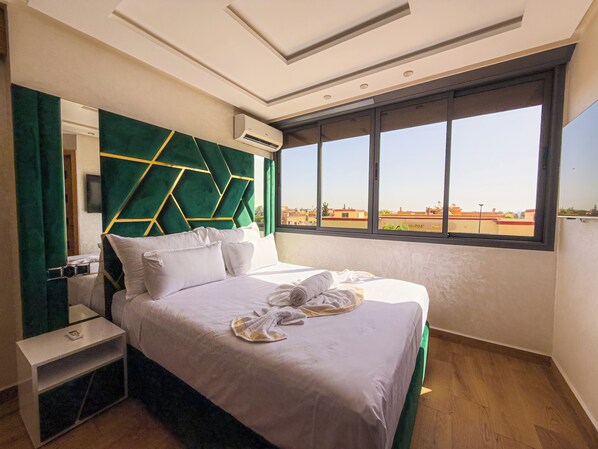 A hotel room with a large bed, a nightstand, a mirror, and a window with a view of buildings.