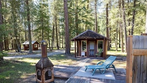 A rustic cabin with a chimney, a covered seating area, and a small deck.