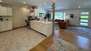 A spacious kitchen with white cabinetry, a central island, and a dining area with a brown sofa.