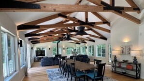 A spacious living area with a wooden ceiling, a dining table with chairs, and a large window.