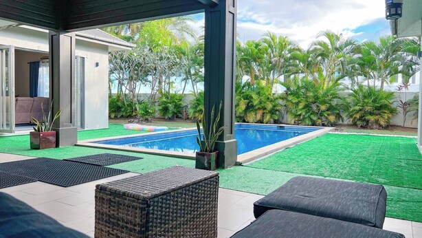 Un espace piscine extérieur moderne offrant une vue dégagée sur une piscine, avec une pelouse artificielle verte et diverses plantes.