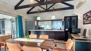 Une cuisine moderne dotée d’un îlot central, d’un coin repas avec une table en bois et des chaises en cuir, et d’un bureau informatique avec un écran.
