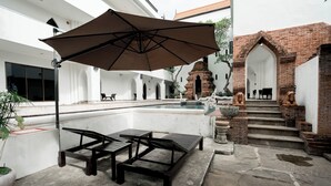 An outdoor seating area with a table and chairs, a large umbrella, and a stone fountain. - Lanna Oriental Mae Rim (Mae Rim)