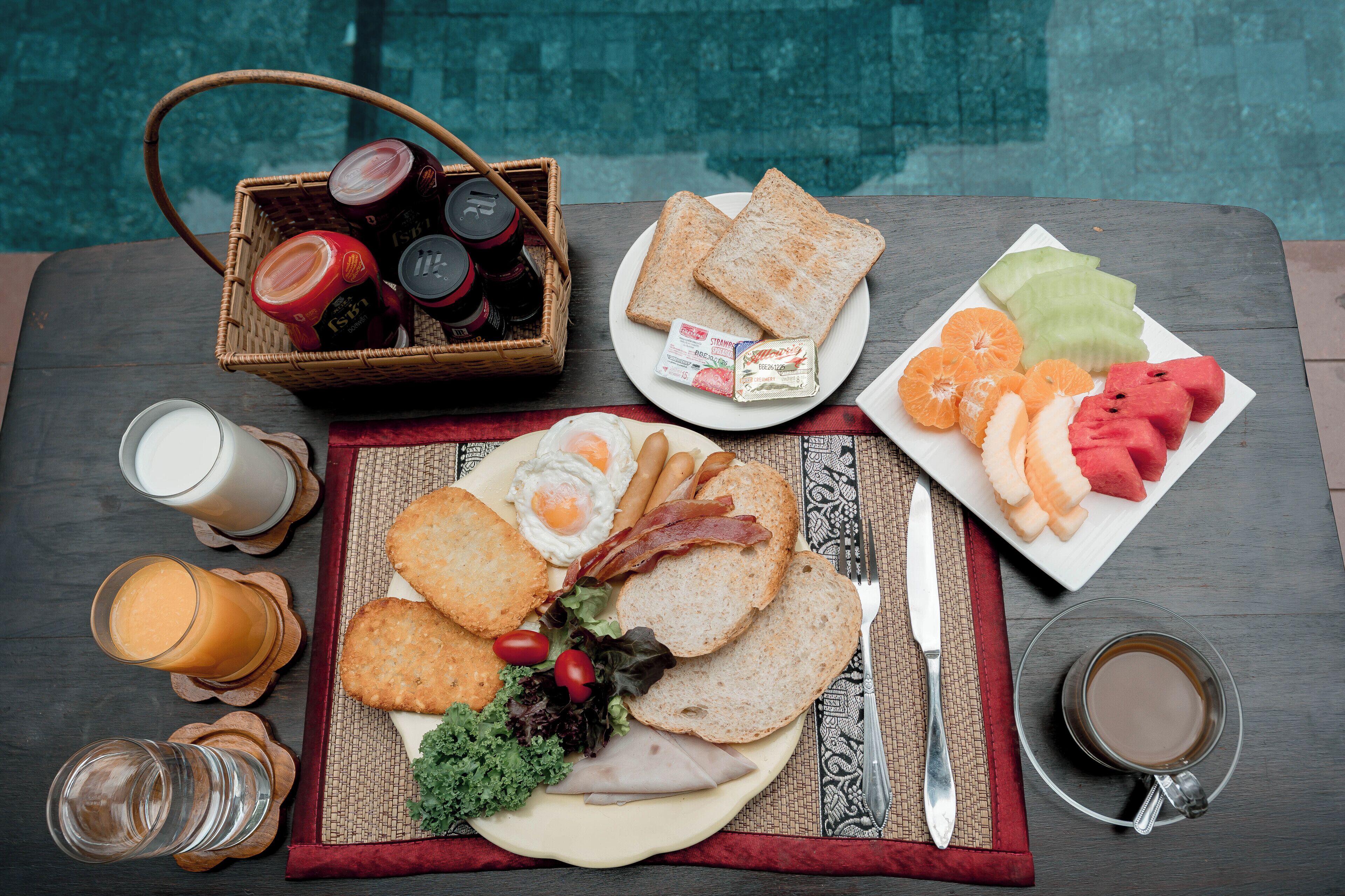 A breakfast table with toast, eggs, bacon, ham, cheese, and various fruits.