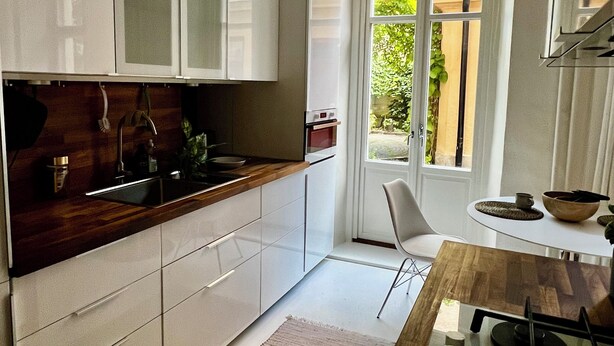 A modern kitchen with white cabinets, a wooden countertop, and a window overlooking a garden. - Cozy turn-of-the-century apartment in Vasastan (Stockholms län)