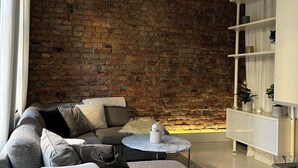 A modern living room with a brick wall, a white sofa, a coffee table, and a white console table with shelves. - Cozy turn-of-the-century apartment in Vasastan (Stockholms län)