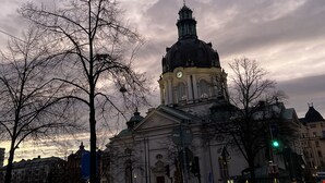 A historic building with a prominent dome and clock tower, surrounded by bare trees and a busy street with buses. - Cozy turn-of-the-century apartment in Vasastan (Stockholms län)