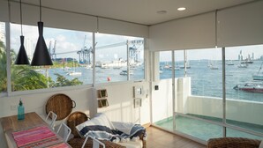 A spacious balcony with a view of the harbor, featuring a wicker chair, a small table with a bottle, and a view of boats and cranes. - Casa Ramona Boutique Rooms (Cartagena)