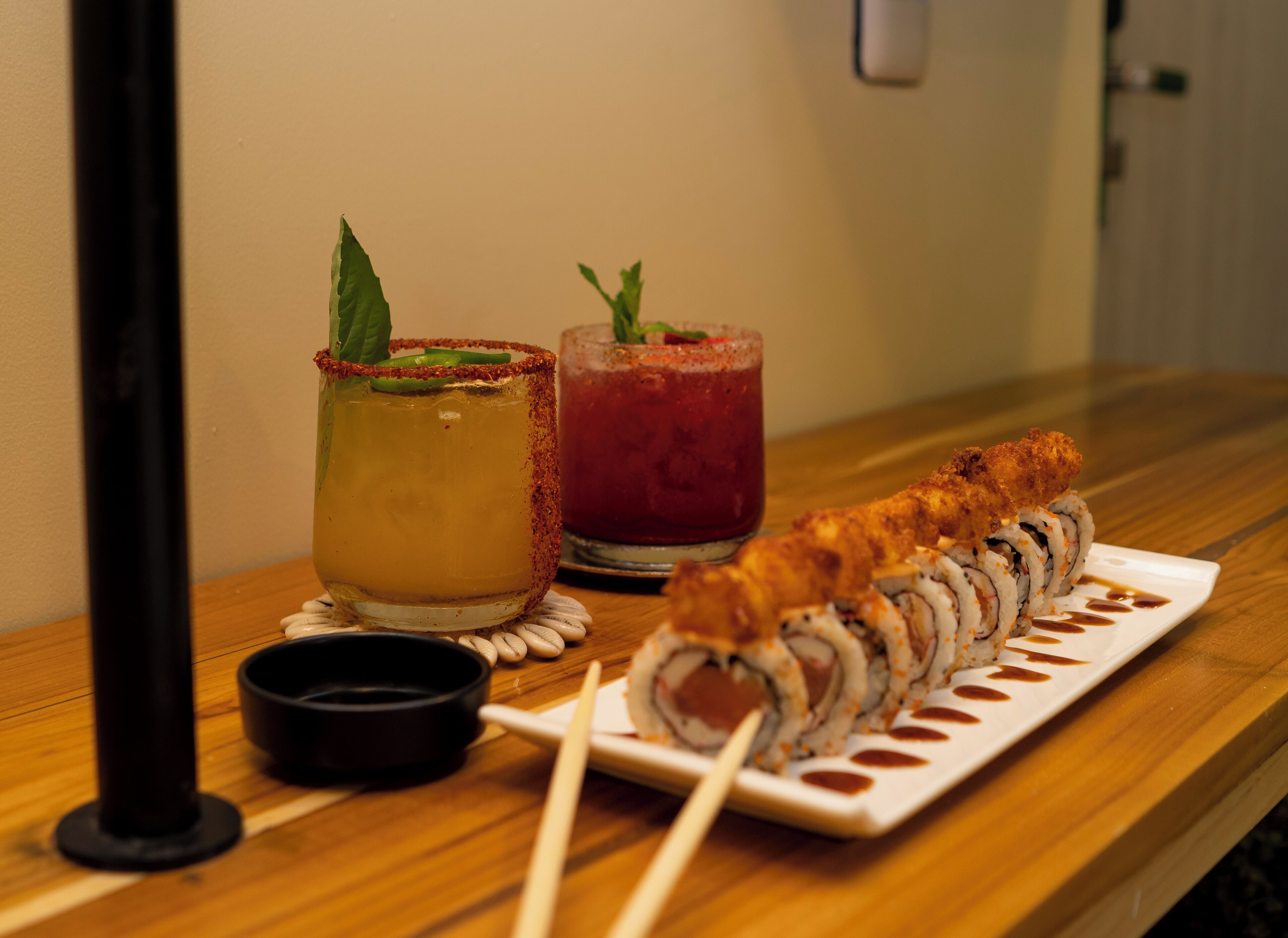 A sushi platter with a dipping sauce and two cocktails on a wooden table.