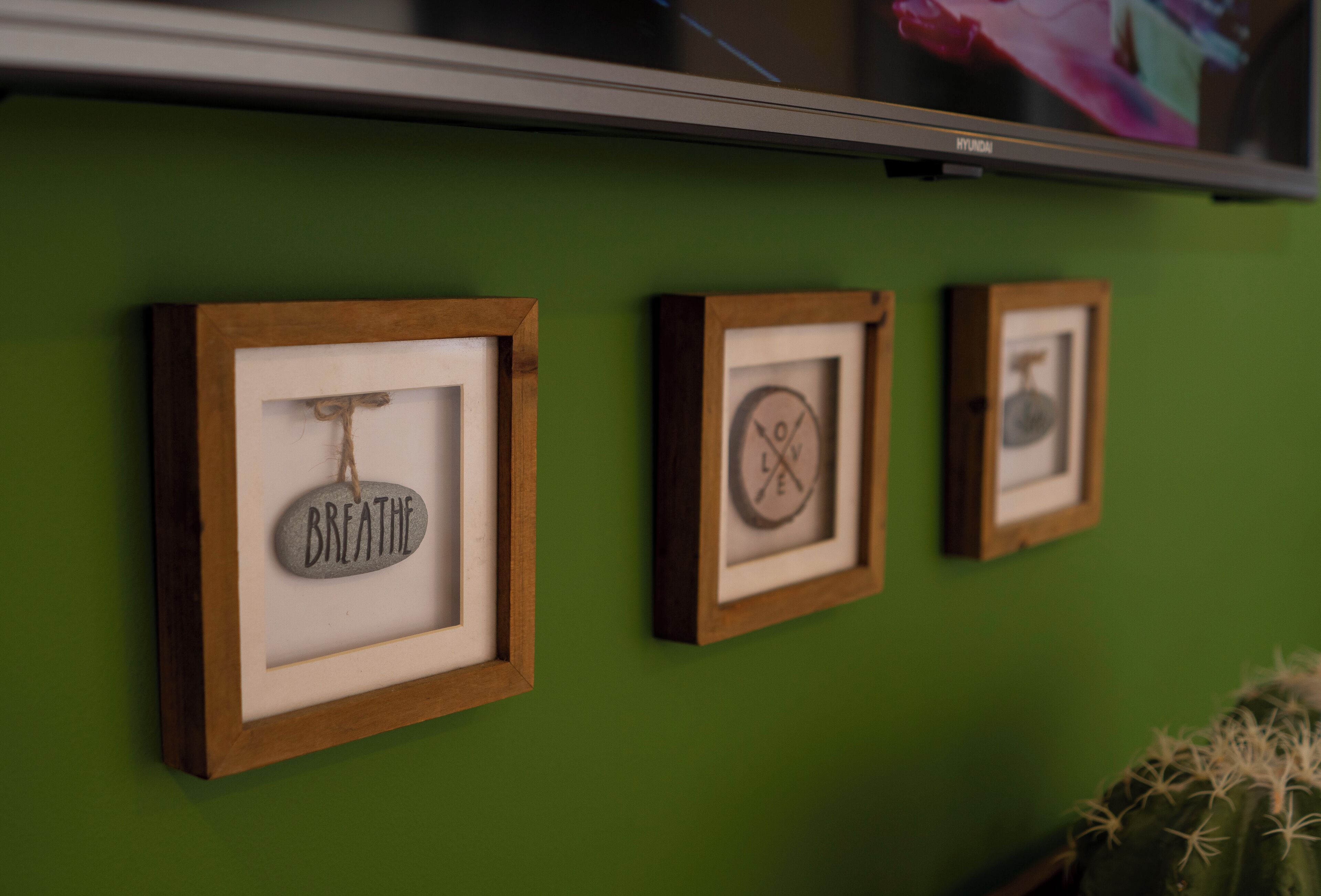 Three framed artworks on a green wall, each with a wooden frame.