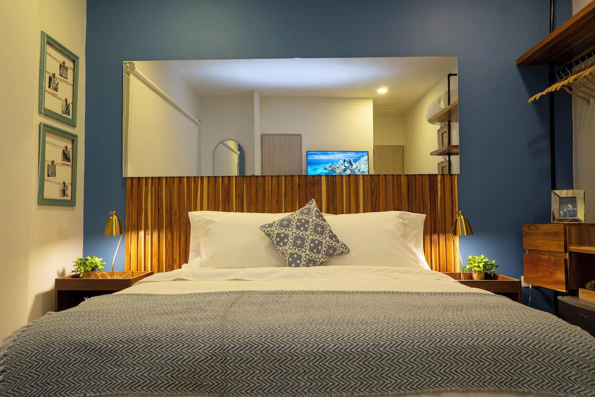 A neatly made bed with a patterned bedspread, a decorative pillow, and a bedside table with a lamp and a small plant.