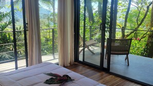 A bedroom with a large bed, a view of lush greenery, and a sliding glass door leading to an outdoor area. - Edge of the World Cabin & Cabana - 10 minutes to Pacific Ocean & On site (Dominical)