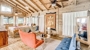 A log cabin interior with a bed, seating area, and a large mirror. - Edge of the World Cabin & Cabana - 10 minutes to Pacific Ocean & On site (Dominical)