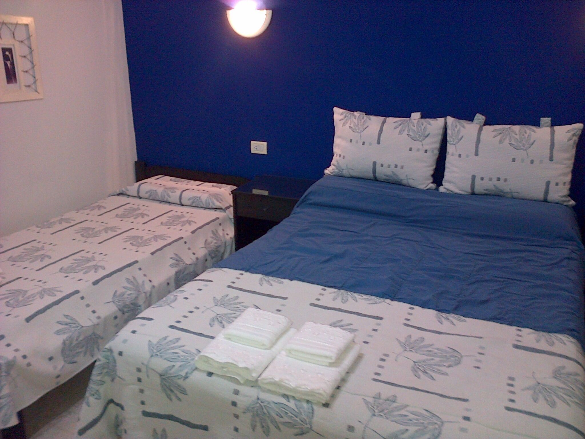Una camera da letto con due letti, ognuno con lenzuola a motivi floreali. Sopra i letti, una lampada fissata al muro.