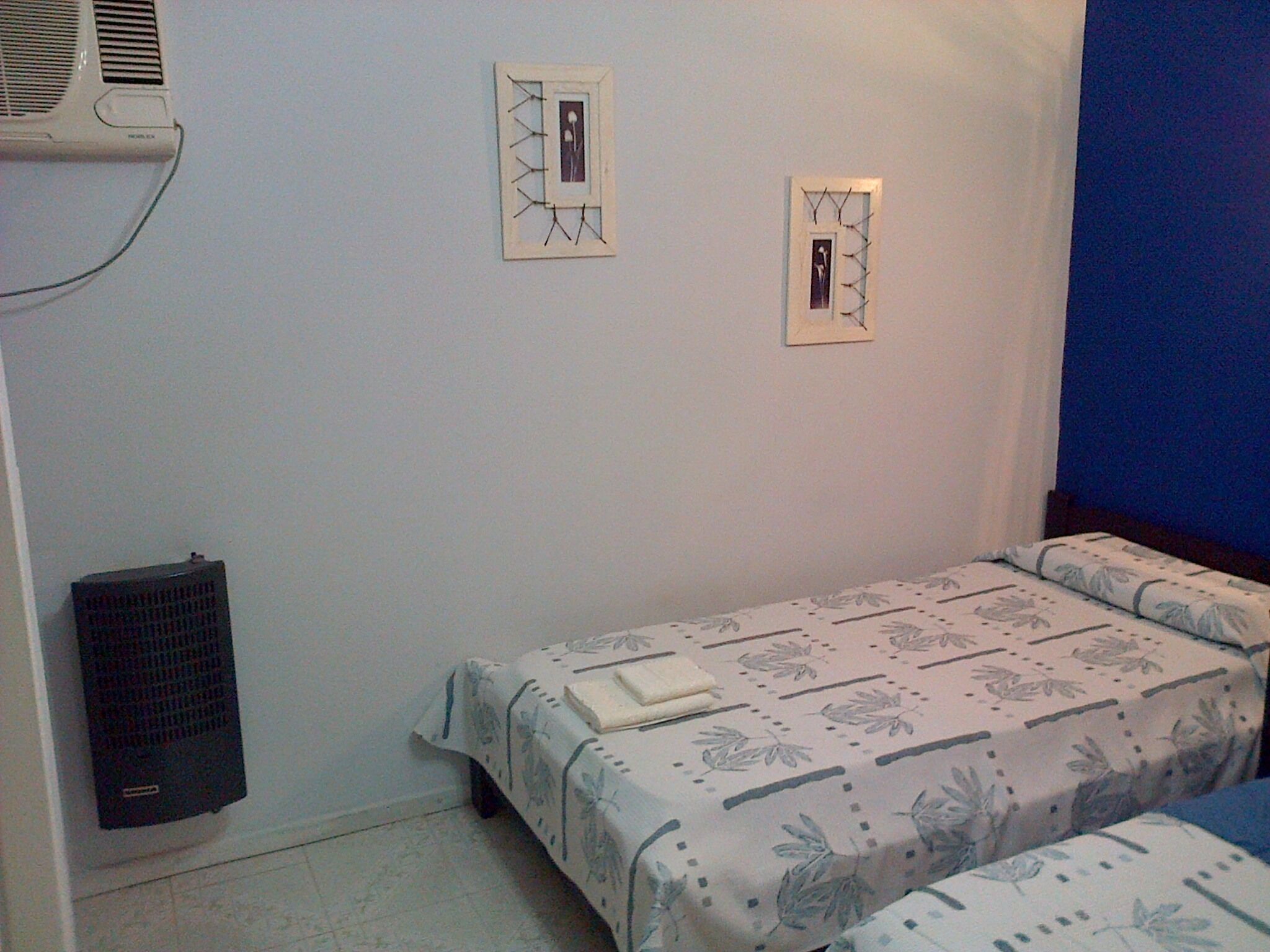 A small, simple room with two beds, a radiator, and two wall-mounted light switches.