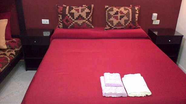 A hotel room with a large bed, two nightstands, and a red wall. - La Posada de Los Fresnos (Colon)