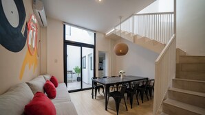 A modern living room with a sofa, red cushions, a dining table with chairs, a staircase, and a large window. - MOT Teatro Soho (Buenos Aires)