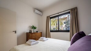 A neatly made bed with folded towels, a wooden dresser with a plant, and a window with curtains. - MOT Teatro Soho (Buenos Aires)