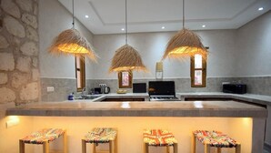 Eine Küche mit einer zentralen Kochinsel, drei hängenden Lampen und vier Stühlen mit bunten Kissen.