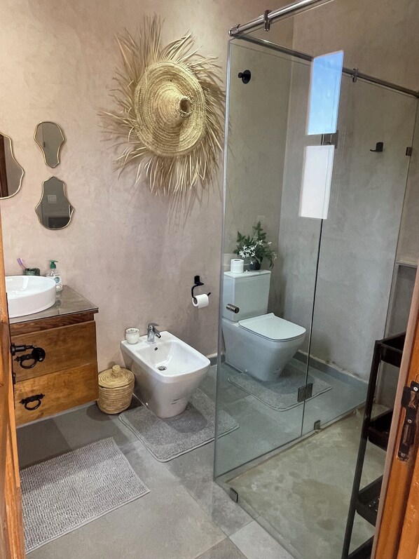 Un baño moderno con cabina de ducha de vidrio, un bidé, un lavamanos y un inodoro.