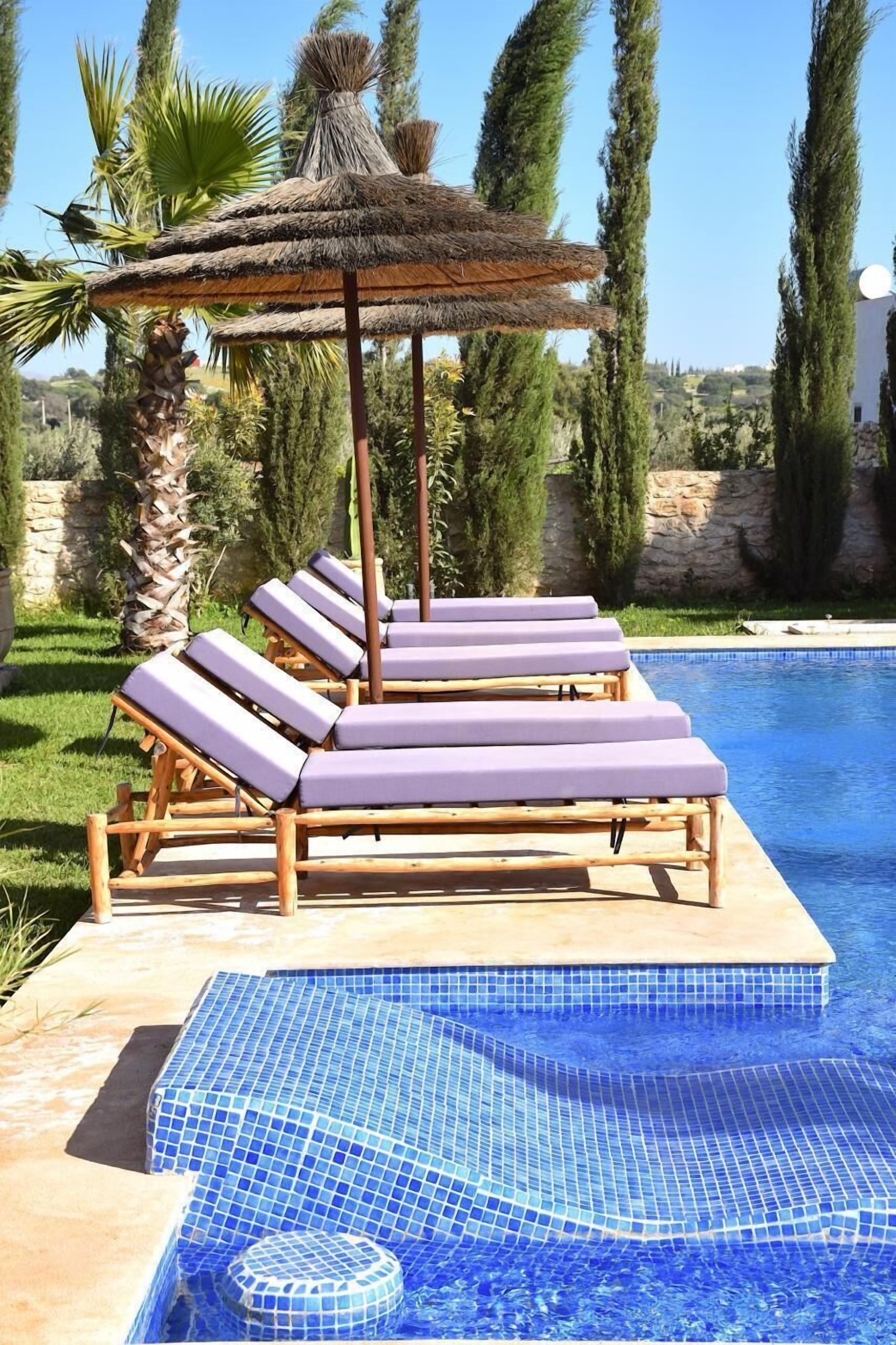 A poolside area with lounge chairs, a thatched umbrella, and a view of the surrounding landscape.