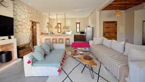 Ein Wohnzimmer mit einer Couch, einem Fernseher, einem Kamin und einer Küche im Hintergrund.
