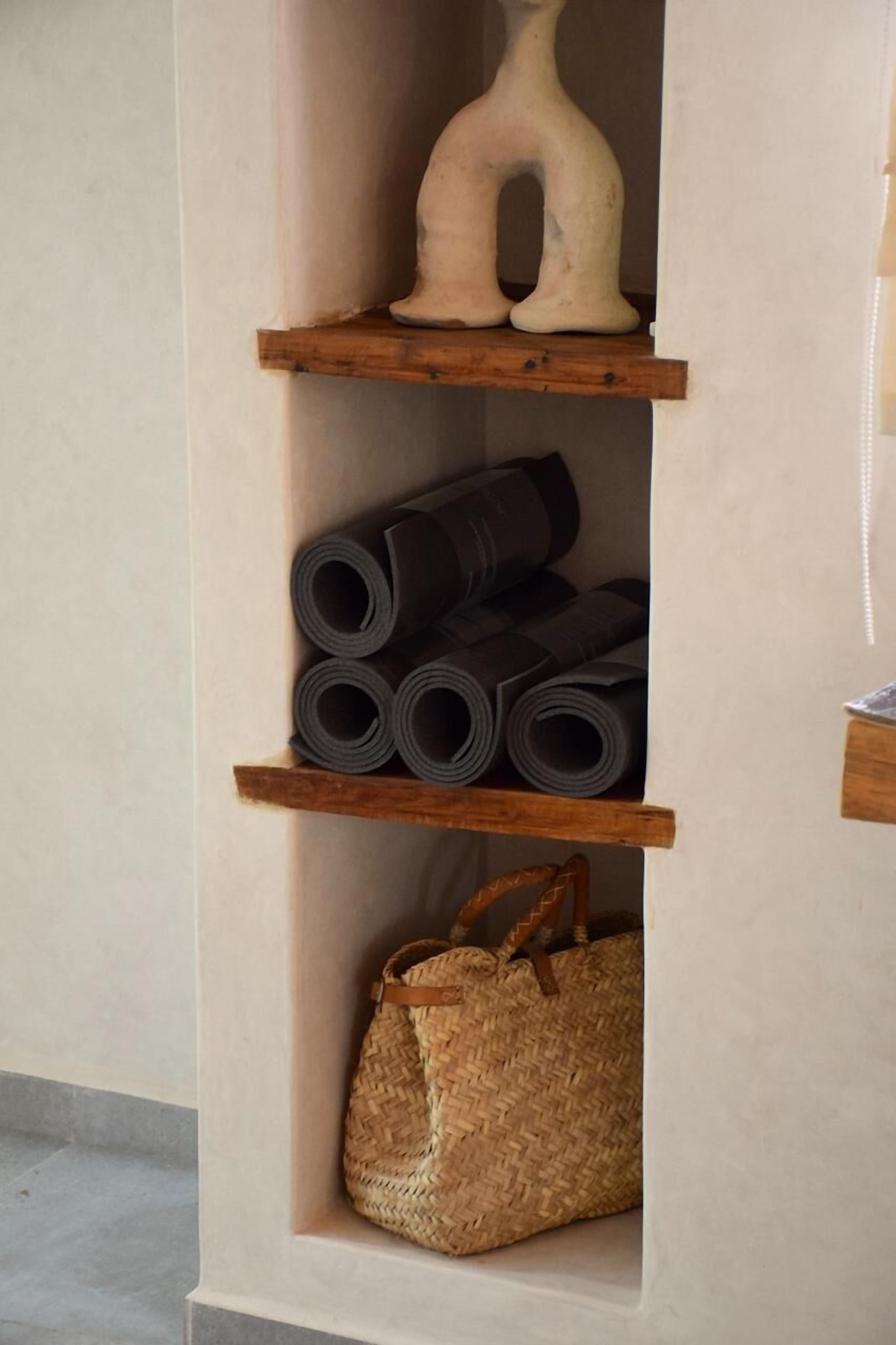 A shelf with rolled-up mats, a woven bag, and a vase.