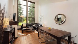 Una sala de estar moderna con un ventanal grande, un sofá de cuero negro, una mesa de comedor de madera y un espejo redondo en la pared.