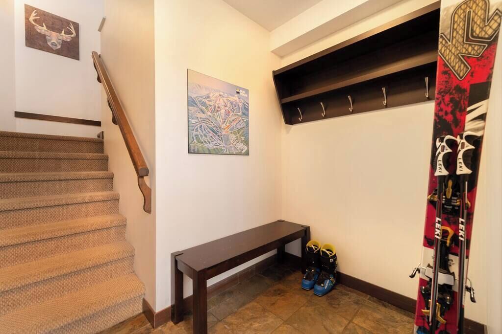 Een trap met een houten leuning, een bankje, een paar ski's en een wandrek met haken.
