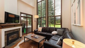 Un salón amplio con chimenea, sofá de cuero y ventanas grandes que ofrecen vistas al exterior.