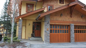 A two-story house with a stone foundation, a yellow facade, and a wooden garage door.