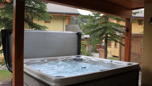 A hot tub under a wooden pergola with a view of a house and trees.