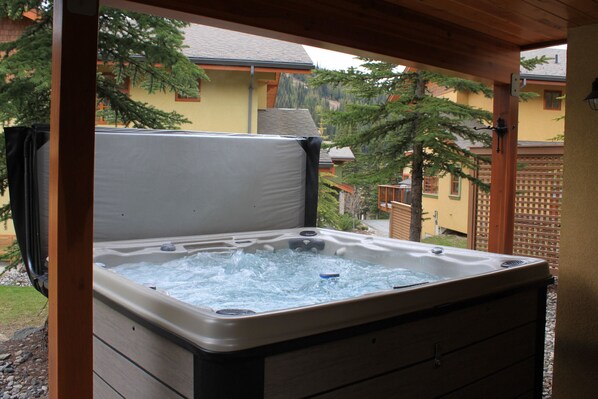 Un bain à remous sous une pergola en bois, avec vue sur une maison et des arbres.
