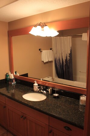 Une salle de bain avec un grand miroir, un lavabo, un robinet, un distributeur de savon et un rideau de douche.